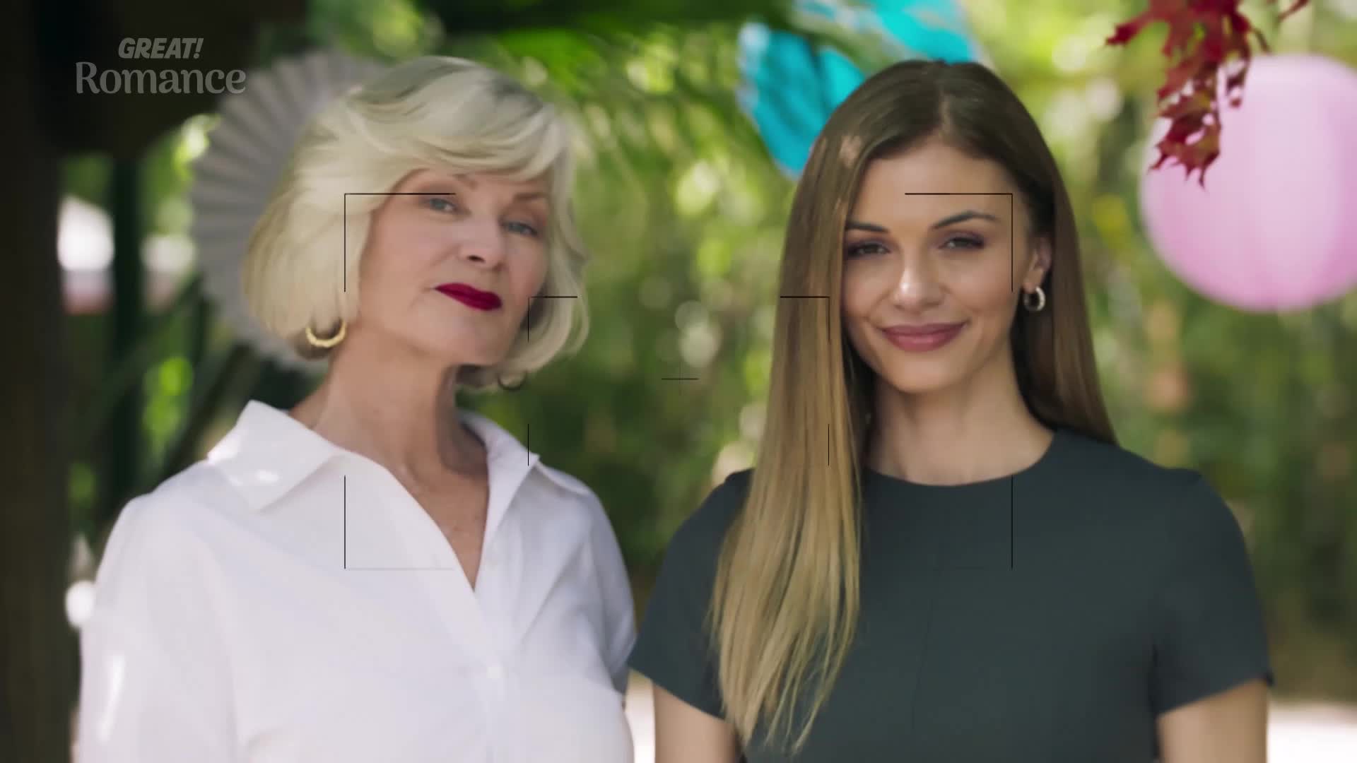 Two women stand posed, one with a stern expression and the other with a gentle smile. A pink balloon bobs gently in the background, hinting at a celebration.