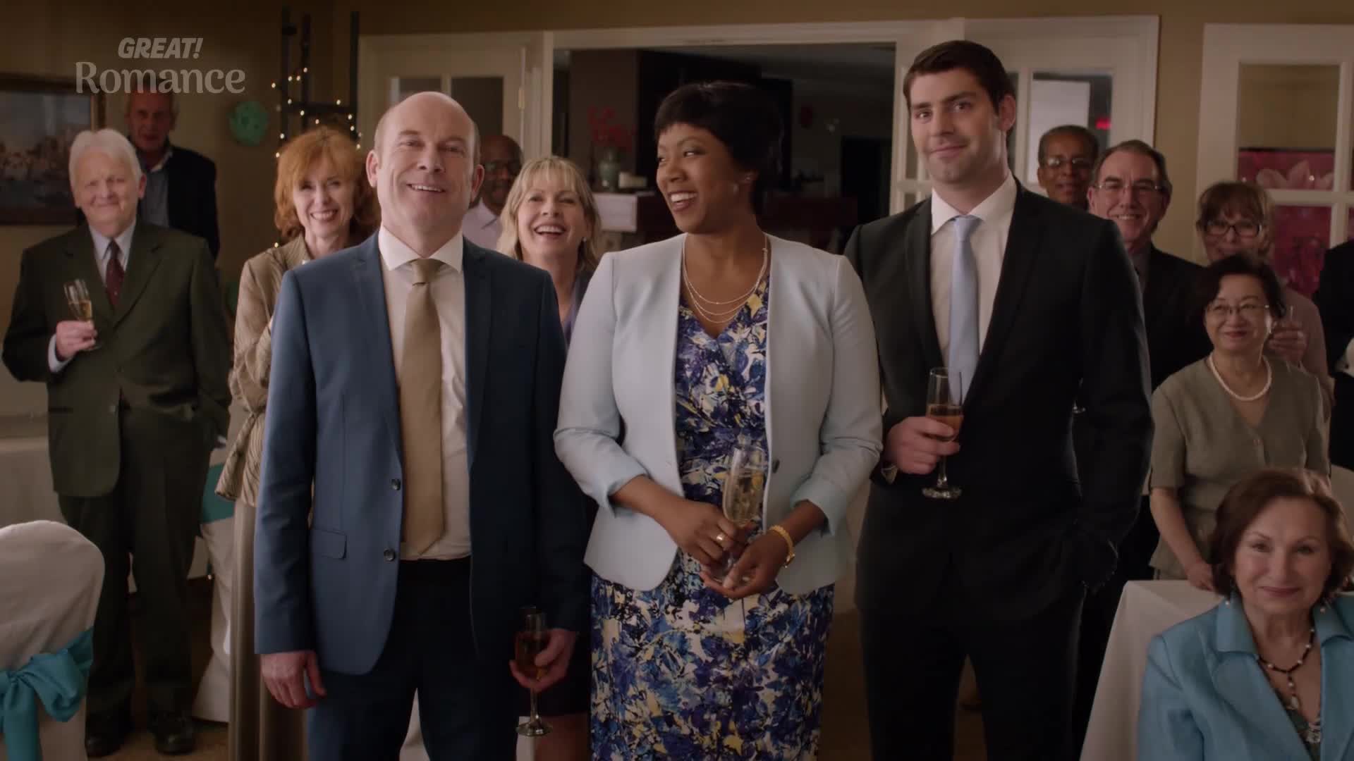 A group of people, dressed smartly for a celebration, stand together holding glasses of champagne. They're all smiling, looking towards the camera as if posing for a photograph.