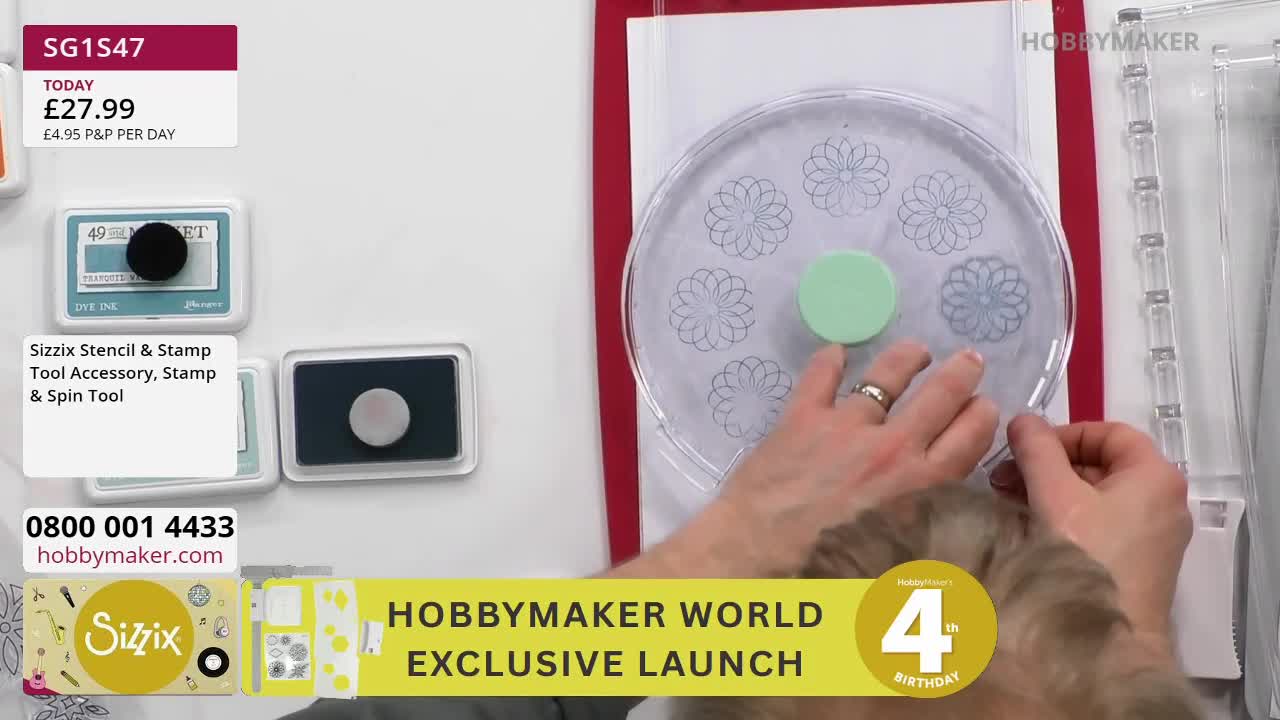 A hand with a ring is placing a light green circular object onto a clear plastic disc with floral stencils. Beside it, two ink pads sit ready for use. A hand with a ring is placing a light green circular object onto a clear plastic disc with floral stencils. Beside it, two ink pads sit ready for use.