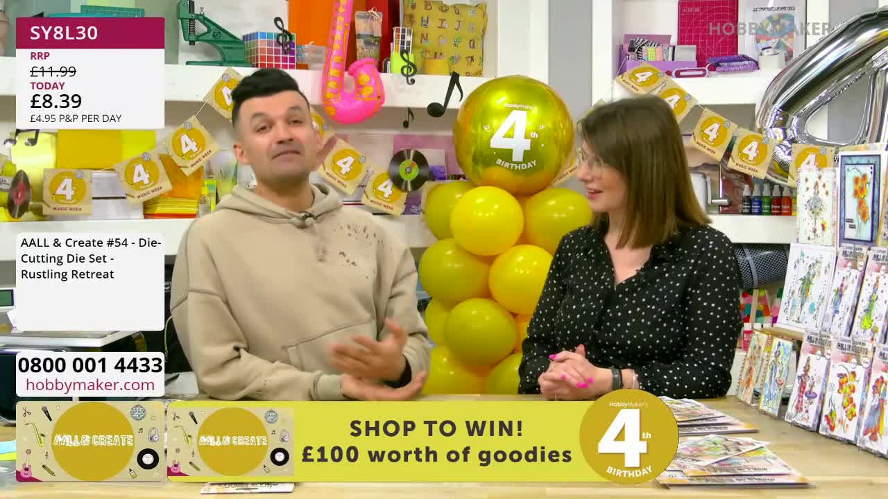 A man in a beige hoodie gestures as he speaks, while a woman in a black polka-dot top looks on. Behind them, a tower of yellow balloons is topped with a large gold balloon featuring the number "4". A man in a beige hoodie gestures as he speaks, while a woman in a black polka-dot top looks on. Behind them, a tower of yellow balloons is topped with a large gold balloon featuring the number "4".