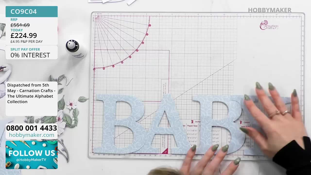 Fingers with pale green polish press down on a light blue letter "B," aligning it with another "B" already placed on the cutting mat. A third letter, an "A," sits just to the left, completing the word "BAB."