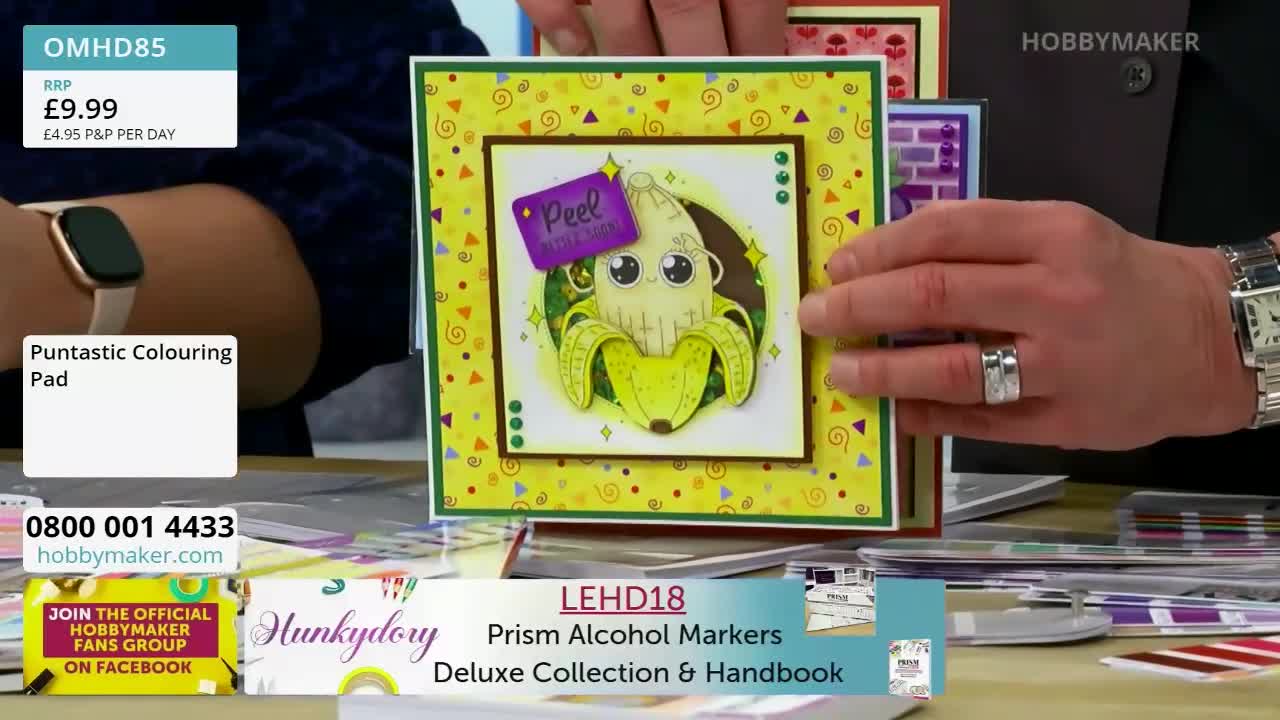 A person's hands are holding up a handmade card featuring a cartoon banana. The card is bright yellow with colourful confetti patterns.