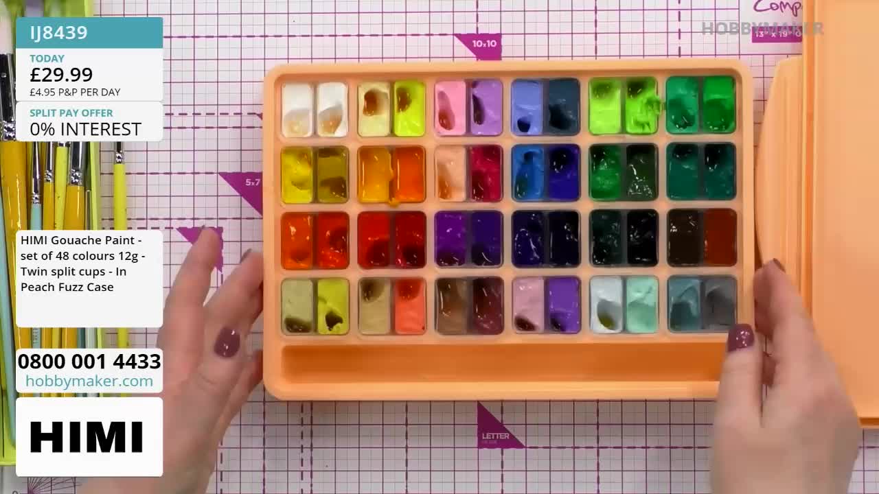 A hand is closing the lid on a bright peach case filled with 48 pans of gouache paint. The individual pans are a vibrant array of colours, neatly arranged in four rows.