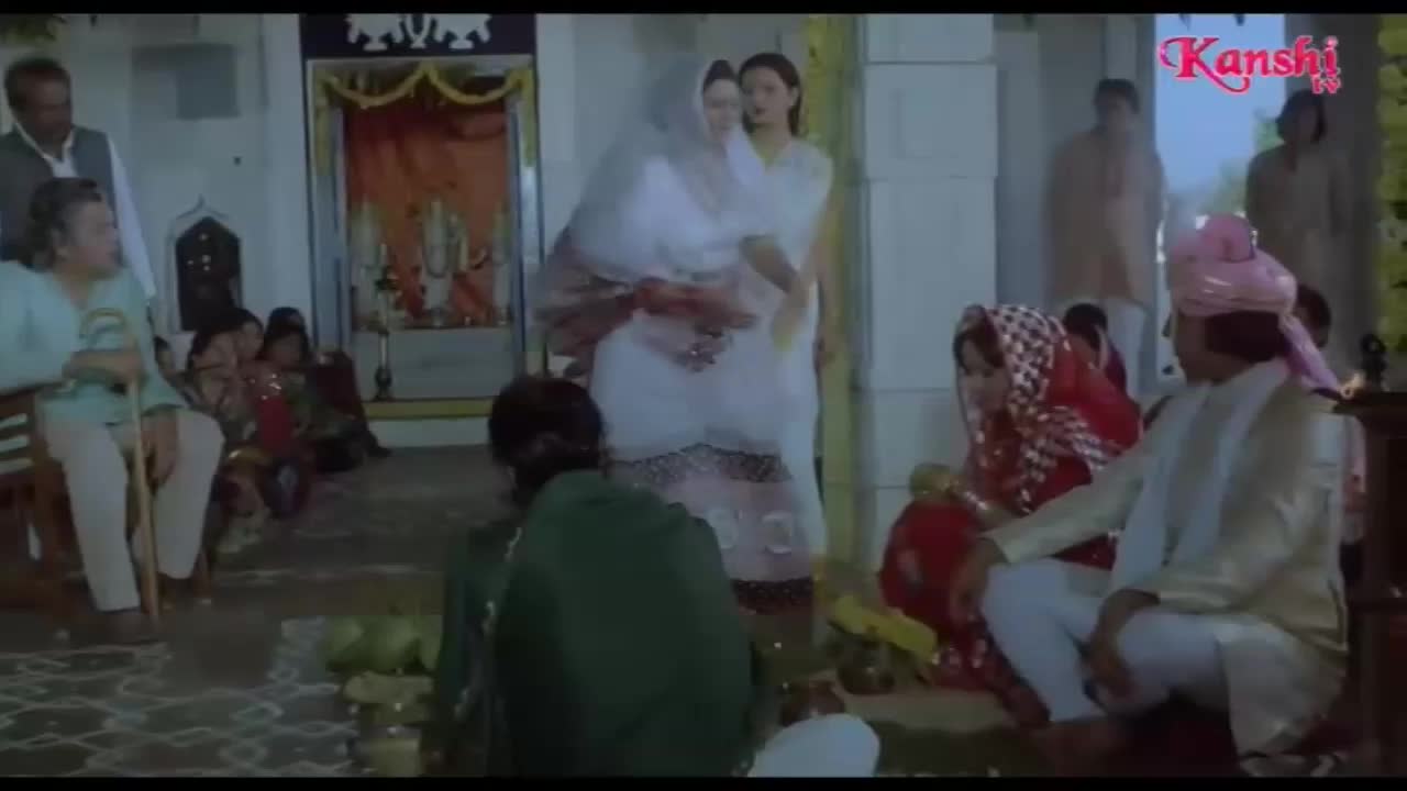 A wedding ceremony is underway, with a bride in a red sari and a groom wearing a pink turban. Several people are gathered, watching the proceedings, with a Kanshi TV logo visible in the corner.