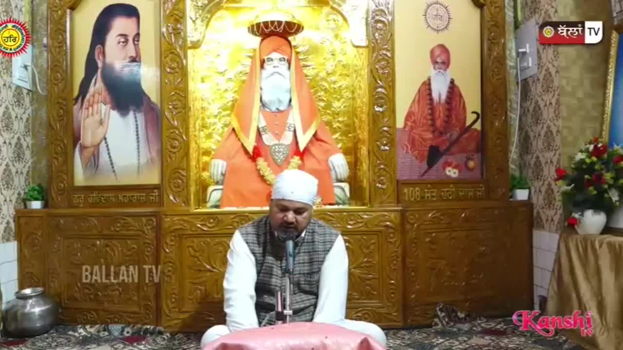 A man in a white turban and vest speaks into a microphone, seated before portraits of religious figures. The scene is broadcast on Kanshi TV, a channel popular in the UK.