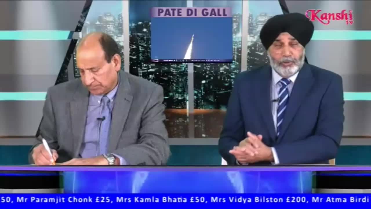 The man on the left is writing on a pad while the man on the right speaks with his hands clasped. A screen behind them displays a rocket launch with the words "PATE DI GALL" above it.