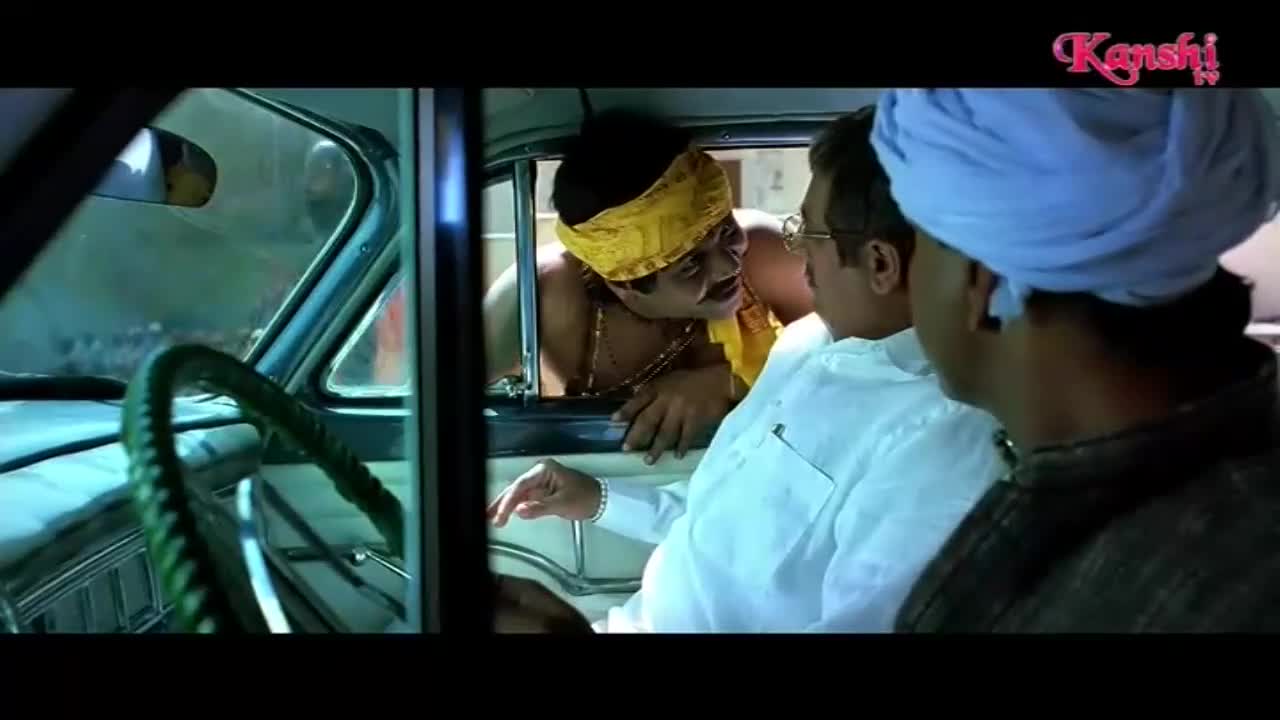 A man in a yellow headdress leans into the car, speaking animatedly to the driver. Another man, wearing a blue turban, sits in the passenger seat, his back to us.