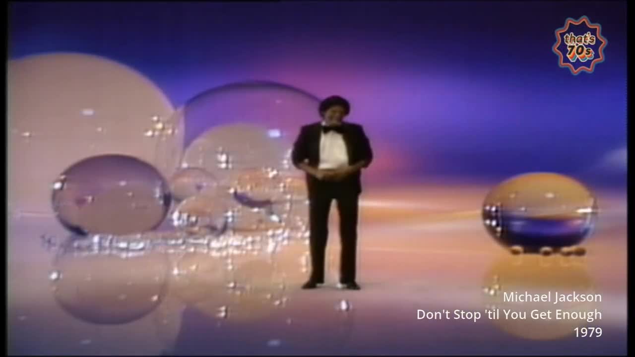 Michael Jackson stands centre stage in a tuxedo, surrounded by enormous, shimmering bubbles. The stage lights reflect off the polished floor and the glass-like spheres.