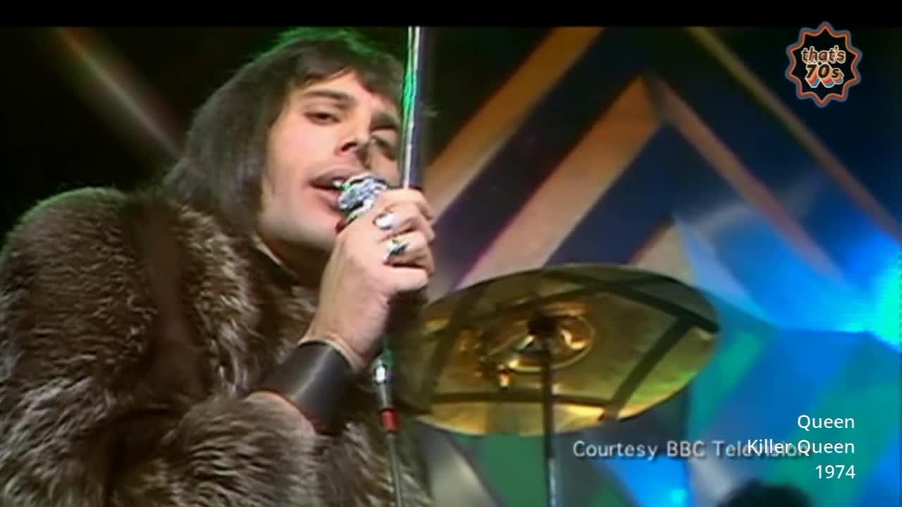 Freddie Mercury, clad in a fur coat, belts into his microphone. A cymbal gleams behind him, catching the stage lights.