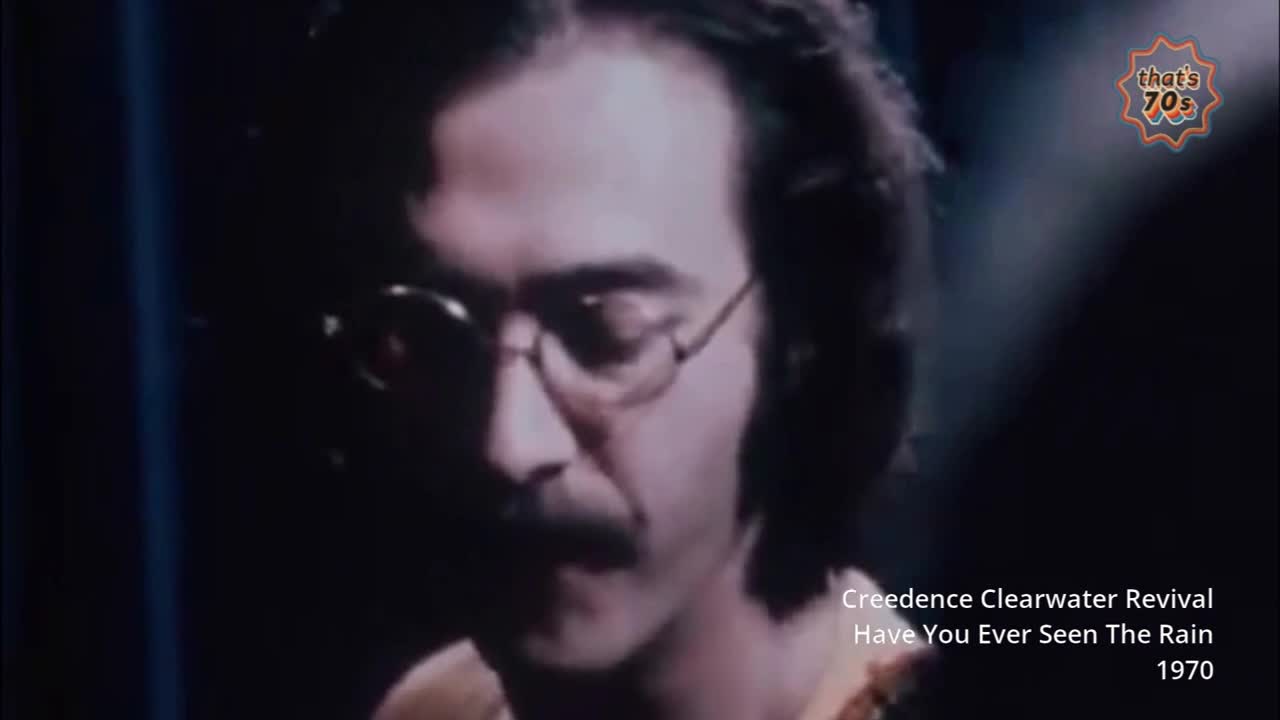 A man with a moustache and round glasses sings into a microphone. The grainy footage is from 1970, a time when Creedence Clearwater Revival was popular.