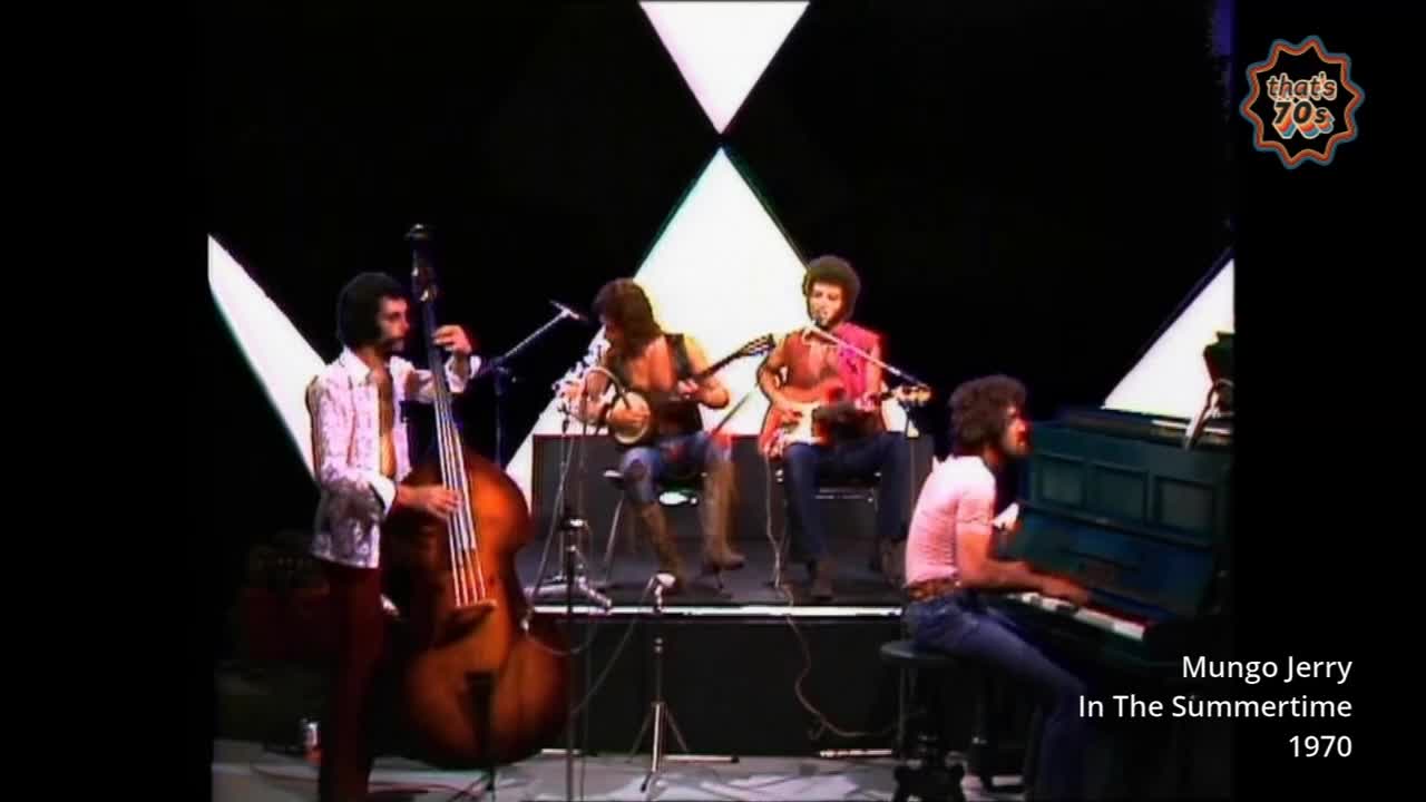 A band plays on a stage, a double bass player standing to the left. The pianist's fingers move across the keys of a dark blue upright piano.