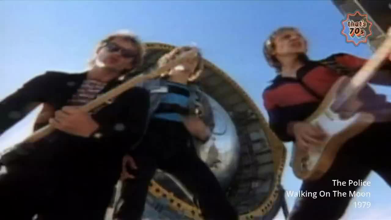 Three blokes are playing guitars, silhouetted against a bright sky. The middle one wears a blue and black striped shirt, while the one on the right has a red and navy striped jumper.