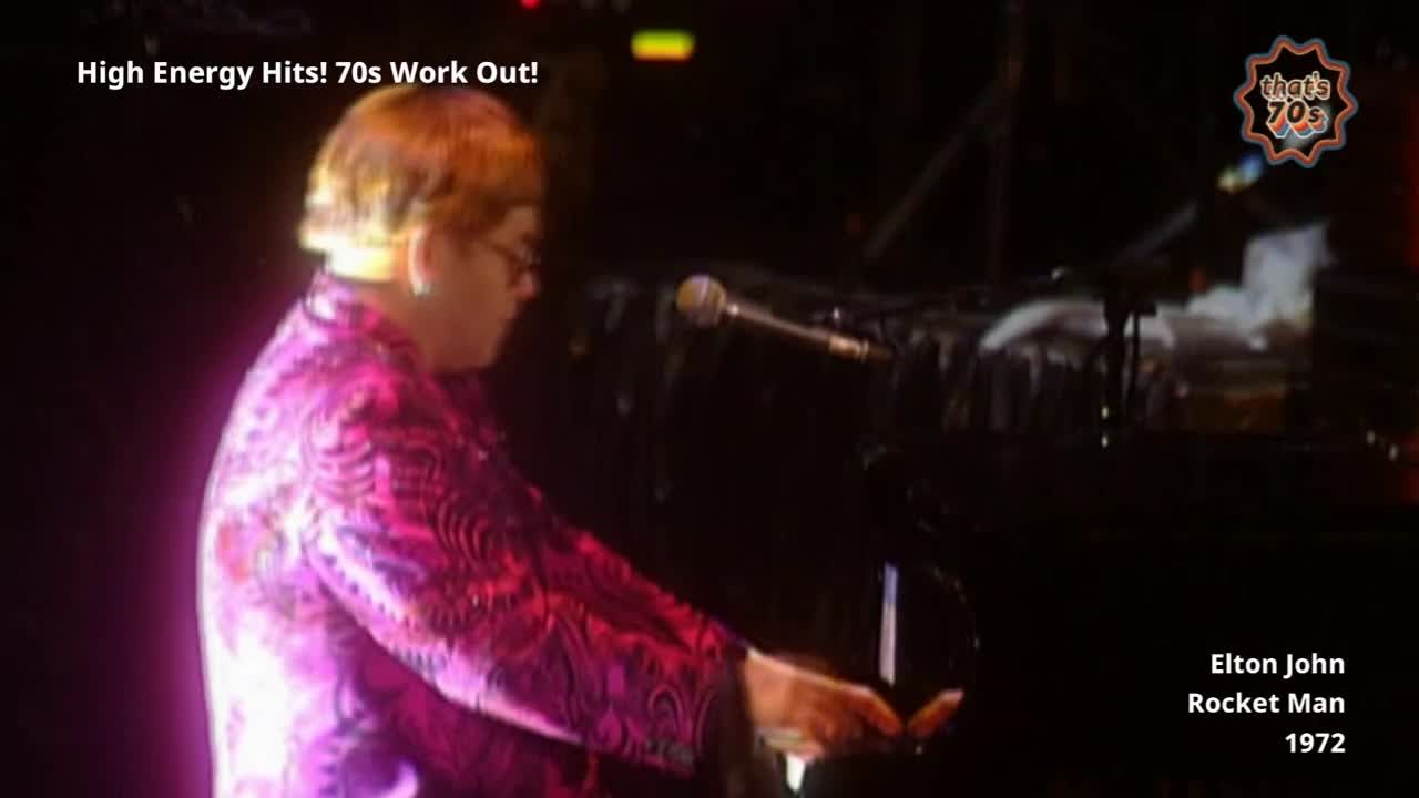 Elton John, in a dazzling pink jacket, plays the piano with focused intensity. His hands move across the keys, a blur of motion against the dark instrument.