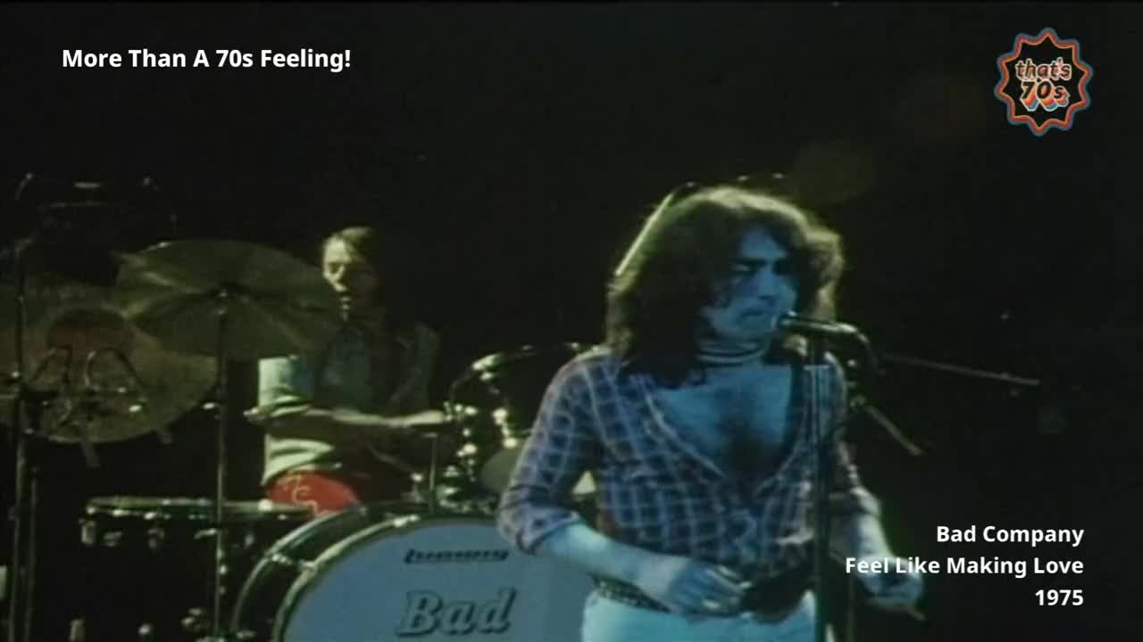 The lead singer, in a plaid shirt, leans into the microphone. Behind him, a drummer is partially obscured by cymbals.