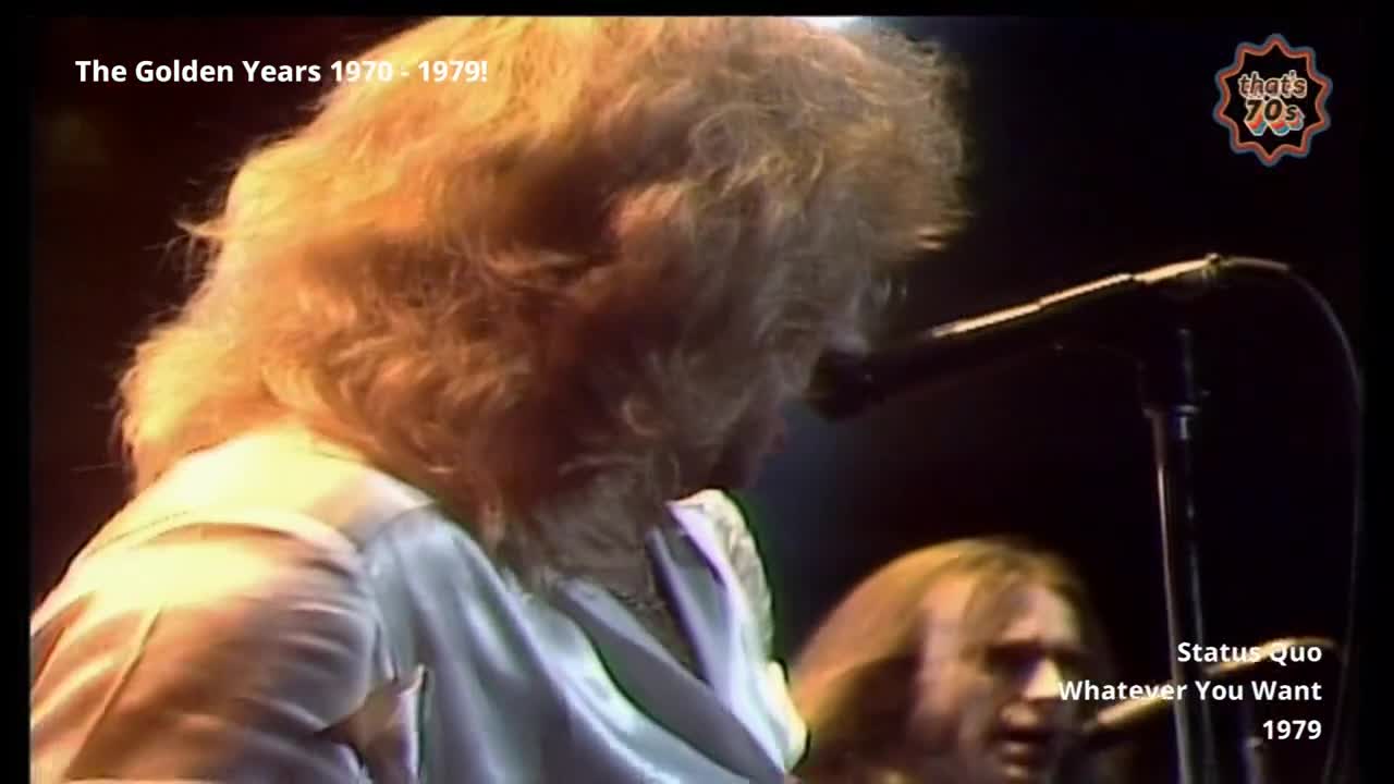 A woman with a cascade of blonde hair leans into a microphone, her satin top catching the stage lights. Behind her, a man with long, light brown hair sings into his own mic.