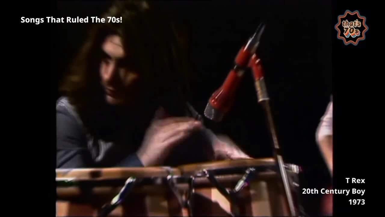 Marc Bolan's hands move quickly over the conga drums, his long hair falling forward. A bright red microphone stands close by, ready for his vocals.