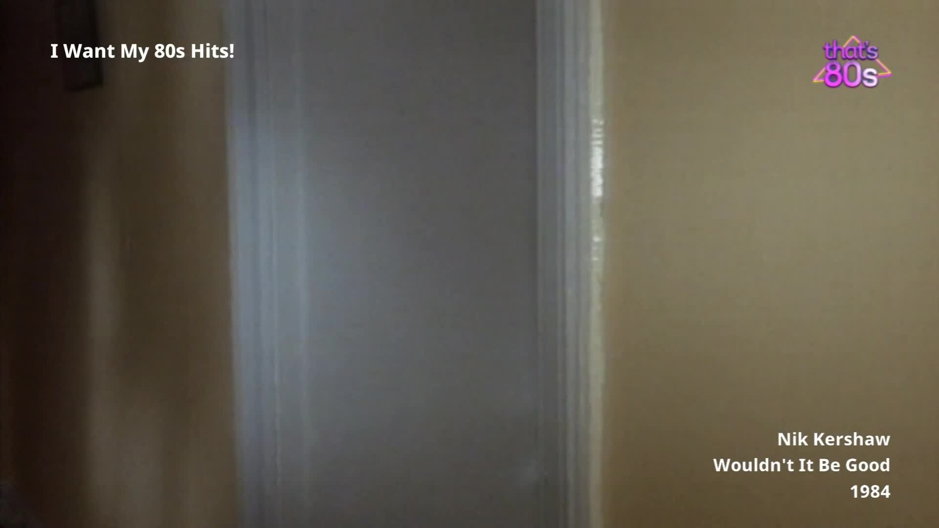 A doorframe stands in a hallway, its white paint chipped and faded. The text "I Want My 80s Hits!" appears in the top left corner, with "Nik Kershaw Wouldn't It Be Good 1984" in the bottom right.
