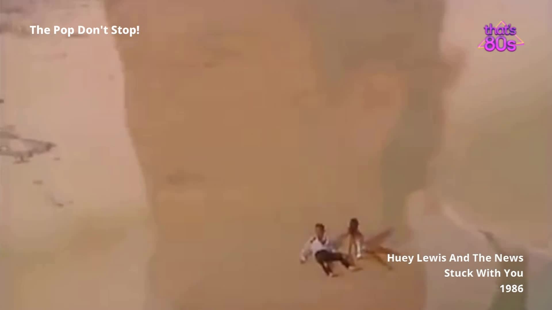 Two figures, one in a white shirt and dark trousers, the other in a light-coloured outfit, are falling through a vast, hazy landscape. The sheer scale of the scene is immense, with what looks like a giant's face looming in the background.