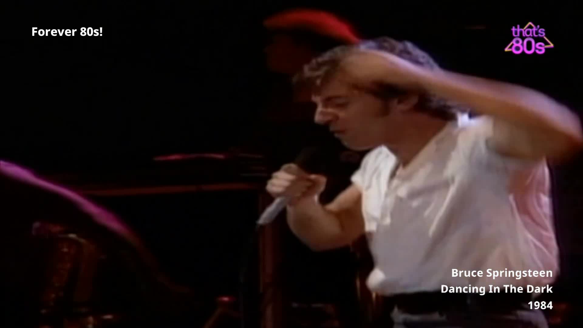 The singer throws his head back, his arm raised as he belts into the microphone. He's on stage, bathed in dim light, mid-song.