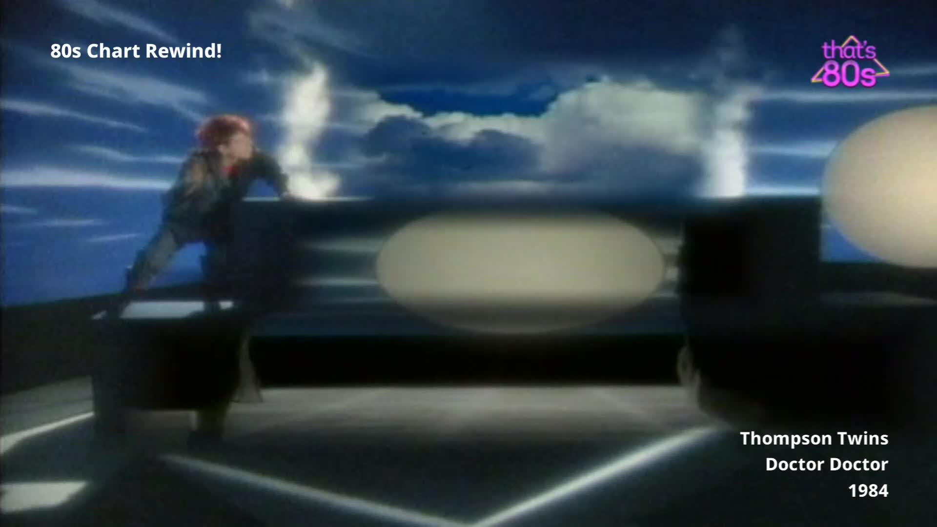 A figure with bright red hair crouches on a dark platform, leaning forward as if to jump. White plumes of smoke erupt around them against a dramatic, cloudy sky.