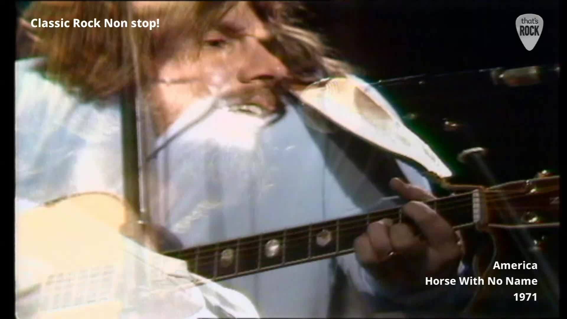 The guitarist's fingers are actively fretting the neck of his acoustic guitar. A microphone hovers close to his mouth as he sings.