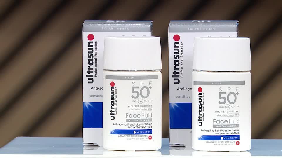 Two bottles of Ultrasun Face Fluid SPF 50 stand on a table, ready for their QVC Beauty presentation. The packaging, with its clean white and blue design, promises advanced Swiss skincare.