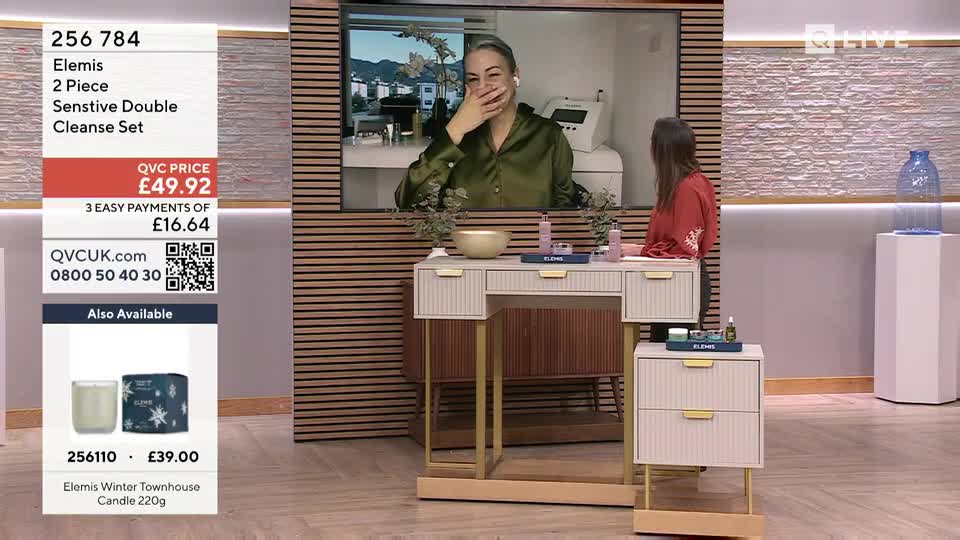 A woman in a green satin top on a screen laughs, covering her mouth. Another woman in a red top sits at a vanity, facing away from the camera.