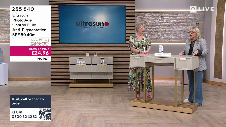 Two women stand behind a desk on a television set, presenting a beauty product. A large screen behind them displays the Ultrasun logo.