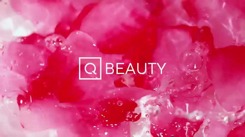 Petals of deep pink and crimson drift through clear, bubbling water. The QVC Beauty logo appears in white text against this vibrant, fluid backdrop.