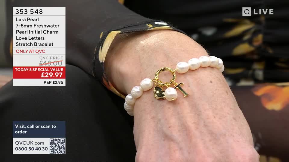 A hand, adorned with a pearl bracelet featuring a gold "T" charm, is held up against a dark, patterned sleeve. On the left, a QVC overlay displays product details and pricing for the Lara Pearl stretch bracelet. A hand, adorned with a pearl bracelet featuring a gold "T" charm, is held up against a dark, patterned sleeve. On the left, a QVC overlay displays product details and pricing for the Lara Pearl stretch bracelet.