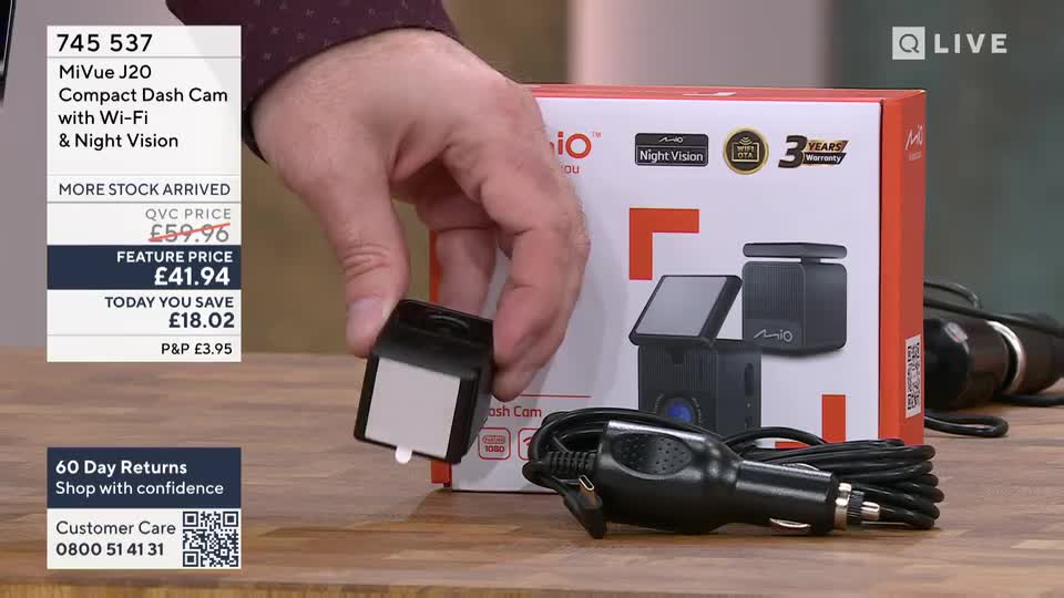 A hand holds up a small black accessory with a white sticker. A dash cam and its car charger lie on the table beside a product box. A hand holds up a small black accessory with a white sticker. A dash cam and its car charger lie on the table beside a product box.