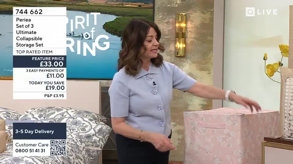 A woman in a light blue blouse gestures towards a pink storage box. The box, patterned with delicate flowers, sits on a surface next to a bed.