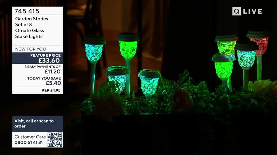 Several ornate glass stake lights glow with vibrant green and blue hues, illuminating a bed of dark foliage. Another light in the background pulses with a warm red.