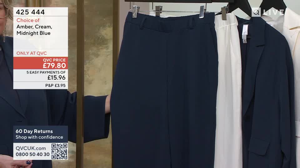 A hand reaches out to adjust a pair of dark blue trousers hanging on a rail. Next to them, a white pair of trousers and a navy blazer are also displayed.