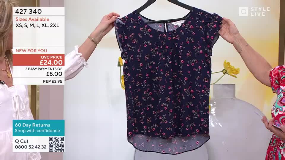 A dark blue blouse with tiny pink flowers is held up for display. The presenter adjusts the sleeve, showing off the delicate flutter.