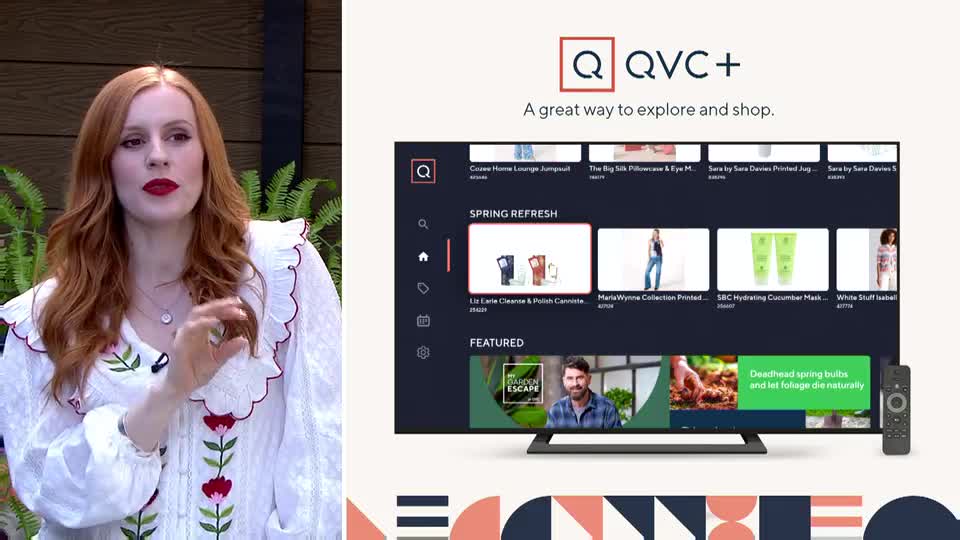 A woman with long red hair, wearing a white blouse with floral embroidery, gestures as she speaks. Beside her, a television displays the QVC+ shopping platform, showcasing various products and featured segments.