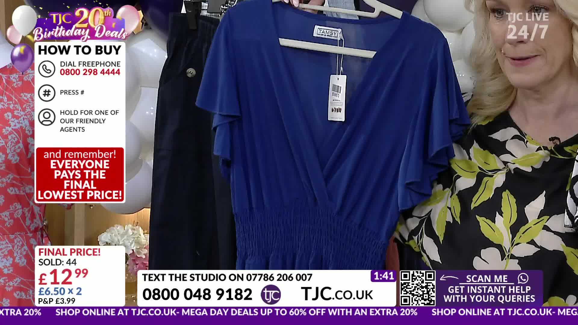 A vibrant blue dress hangs on display, its ruffled sleeves catching the light. A woman in a floral top smiles as she stands beside it.