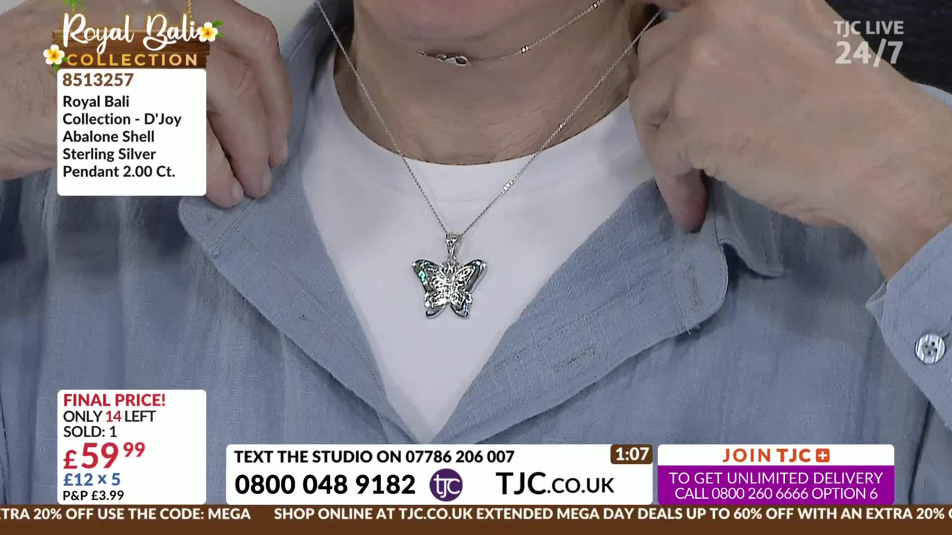 A hand adjusts the delicate chain of a sterling silver butterfly pendant. The necklace, featuring abalone shell accents, rests against a pale blue shirt.