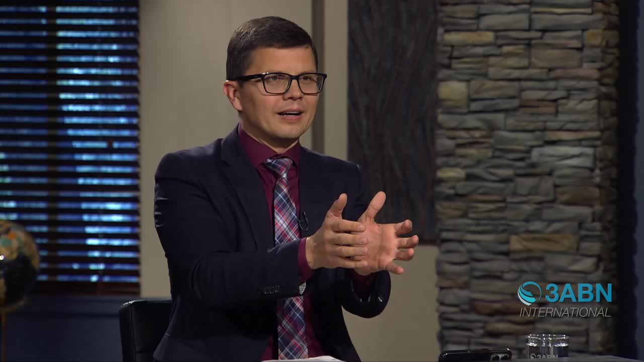 A man in a dark suit and tie gestures with his hands while speaking. He's seated in front of a stone column, with a 3ABN International logo visible.