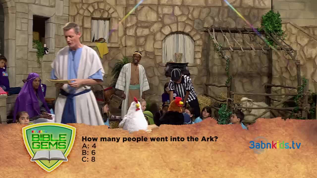 A man in a white robe reads from a card, while costumed figures and children sit nearby. A chicken puppet is perched on a fuzzy, brown surface in front of a group of kids.
