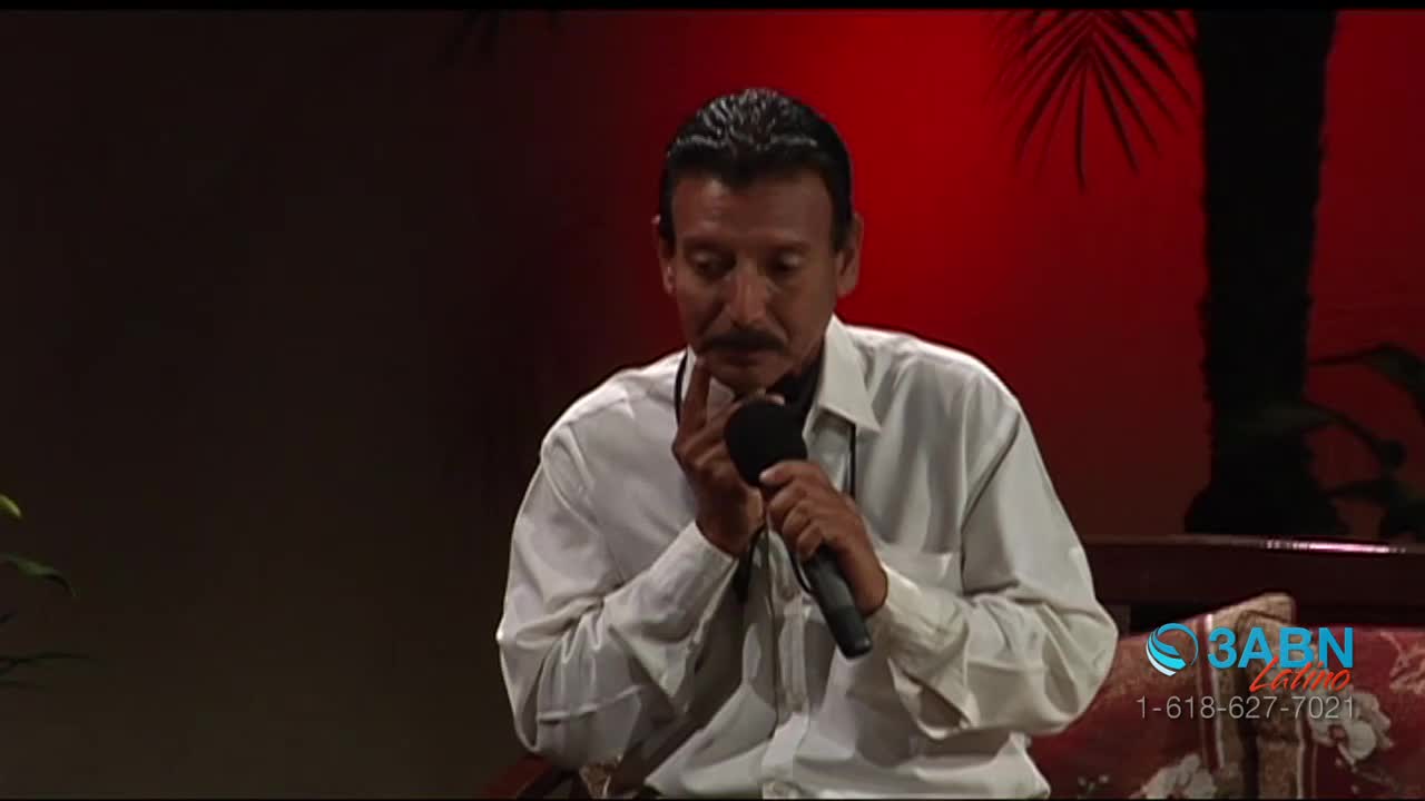 A man in a white shirt holds a microphone, his fingers touching his chin as he speaks. The 3ABN Latino logo is visible in the corner, and the background is a deep red.
