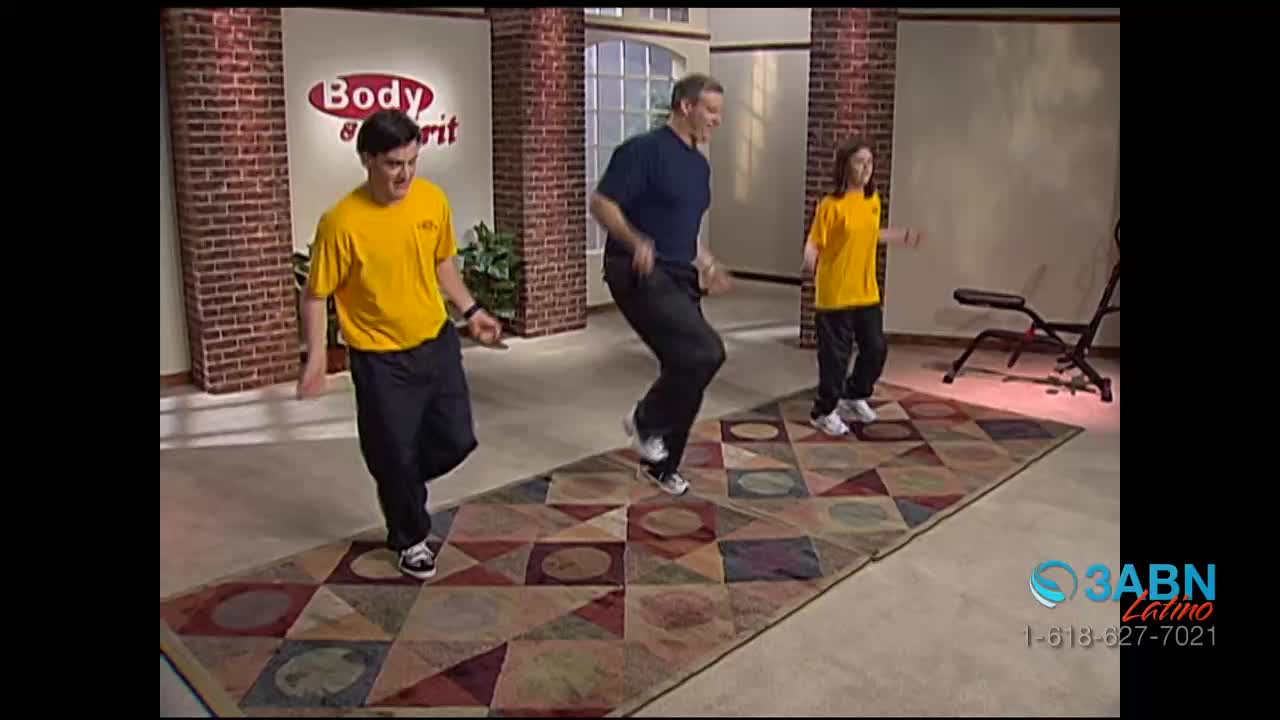 Three people in workout clothes are bouncing on a patterned rug, moving their arms as they lift their knees. The scene is a television program from 3ABN Latino, with a "Body & Spirit" logo visible.
