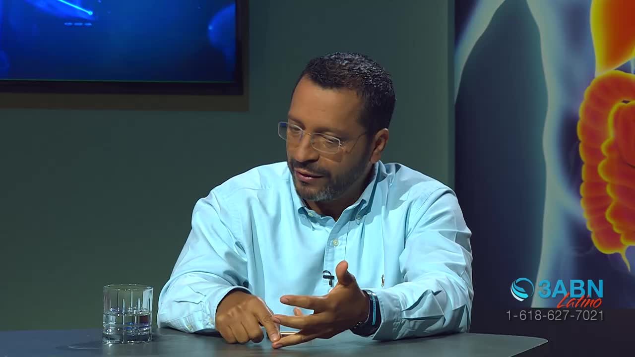 A man in a light blue button-down shirt leans forward, gesturing with his hands as he speaks. Behind him, a graphic displays what appears to be an anatomical illustration, with the 3ABN Latino logo visible in the corner.