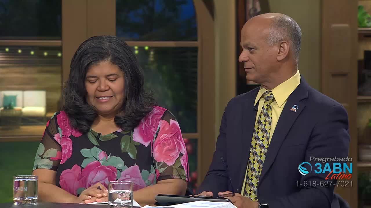 A woman with dark, wavy hair and a floral dress looks down, her hands clasped. Beside her, a man in a suit and yellow tie glances away, speaking. A logo for 3ABN Latino appears in the corner.