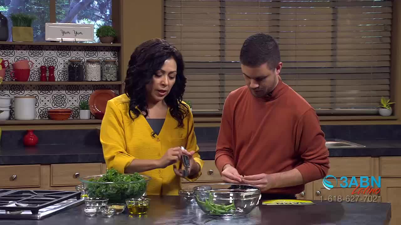 A woman in a yellow shirt is holding a small silver object over a bowl of leafy greens. Next to her, a man in an orange shirt is carefully separating small pieces of food. The 3ABN Latino logo is visible in the lower right corner.