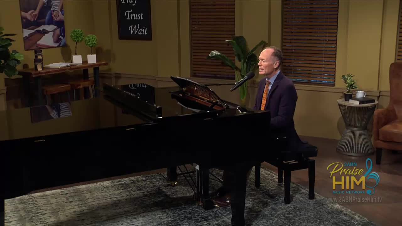 A man in a suit sits at a grand piano, singing into a microphone. The 3ABN Praise Him Music Network logo is visible in the corner.
