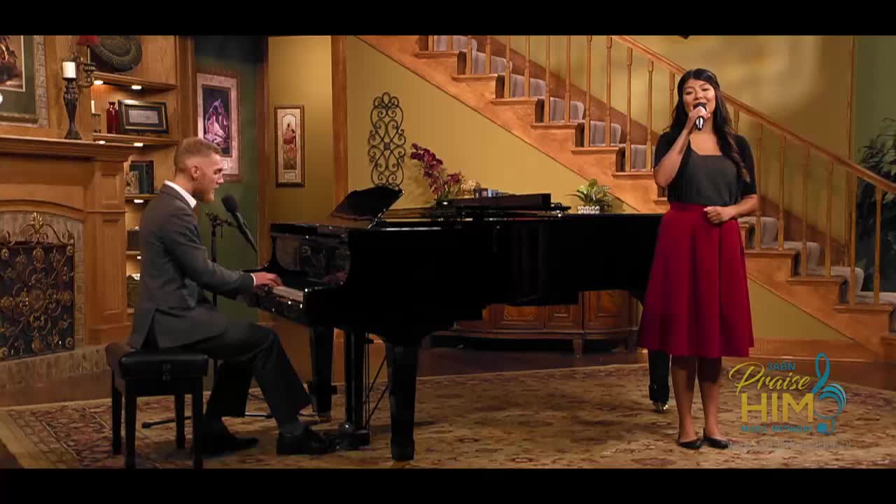 A woman in a red skirt stands center stage, singing into a microphone. A man in a suit plays the piano to her left, the music flowing from the keys.
