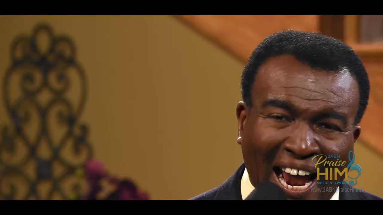 A man in a dark suit is speaking into a microphone, his mouth wide open in a joyful expression. The 3ABN Praise Him Music Network logo is visible in the corner.
