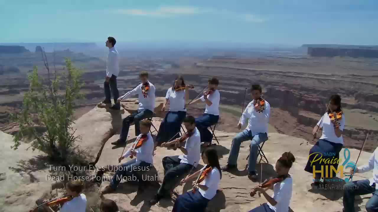 On a rocky overlook in Utah, a group of musicians plays violins. They're part of a 3ABN Praise Him Music Network production, with a vast canyon stretching out behind them.
