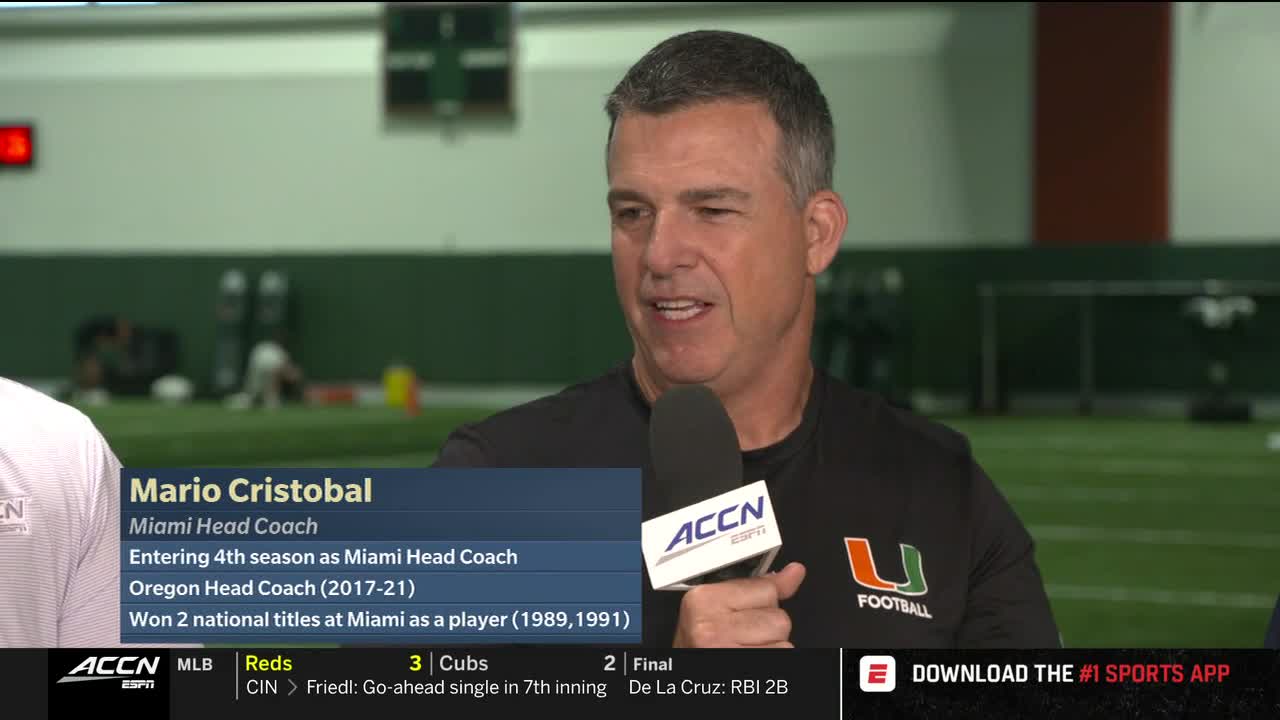 Mario Cristobal, the Miami head coach, is speaking into a microphone, likely for the ACC Network. A graphic on the screen details his coaching history and playing career.
